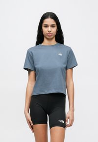 Frau mit langen dunklen Haaren, die ein blaues kurzes T-Shirt und schwarze Radsport-Shorts trägt, beide mit "The North Face"-Logos.