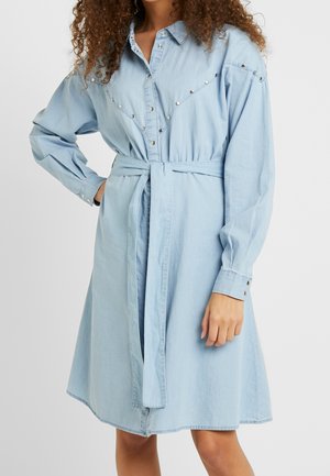 Robe en denim bleu clair avec des manches longues, des poignets boutonnés, une taille ceinturée et des clous métalliques le long du devant et des épaules.