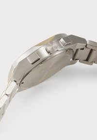 Edelstahl-Uhr mit rundem Gehäuse, silbernem Armband und goldenen Akzenten auf der Lünette. Verfügt über Tasten und einen unbeschrifteten, glatten Rücken.