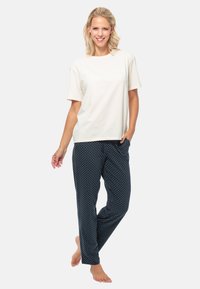 Ensemble de pyjama en coton comprenant un t-shirt à manches courtes crème et un pantalon bleu marine à pois blancs, avec poches latérales et coupe décontractée.