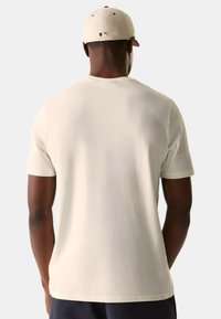 Camiseta beige claro, de mangas cortas, material de algodón suave, cuello redondo, diseño liso y corte relajado, llevada con una gorra de color claro.