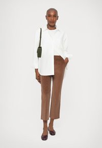 Weißes Button-up-Hemd, braune Cordstoff-Hosen in Cropped-Länge, dunkel-rotbraune Ballerinas und eine kleine grüne Umhängetasche mit glatter Textur und lässigem Schnitt.