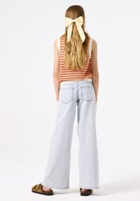 Lichtblauwe wijde jeans met achterzakken, gecombineerd met een oranje en crèmekleurige gestreepte gebreide tanktop en bruine instapsandalen. Lang, golvend haar vastgebonden met een gele strik.