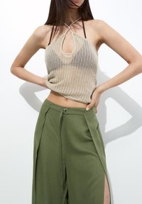 Haut en tricot beige à col halter avec un design à œillet, associé à un pantalon vert taille haute avec des fentes latérales et un accent en métal argenté.