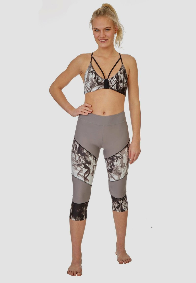 Sportieve croptop in zwart-wit abstracte print met een bandjesdesign, gecombineerd met grijze leggings met zwarte accenten en patronen.