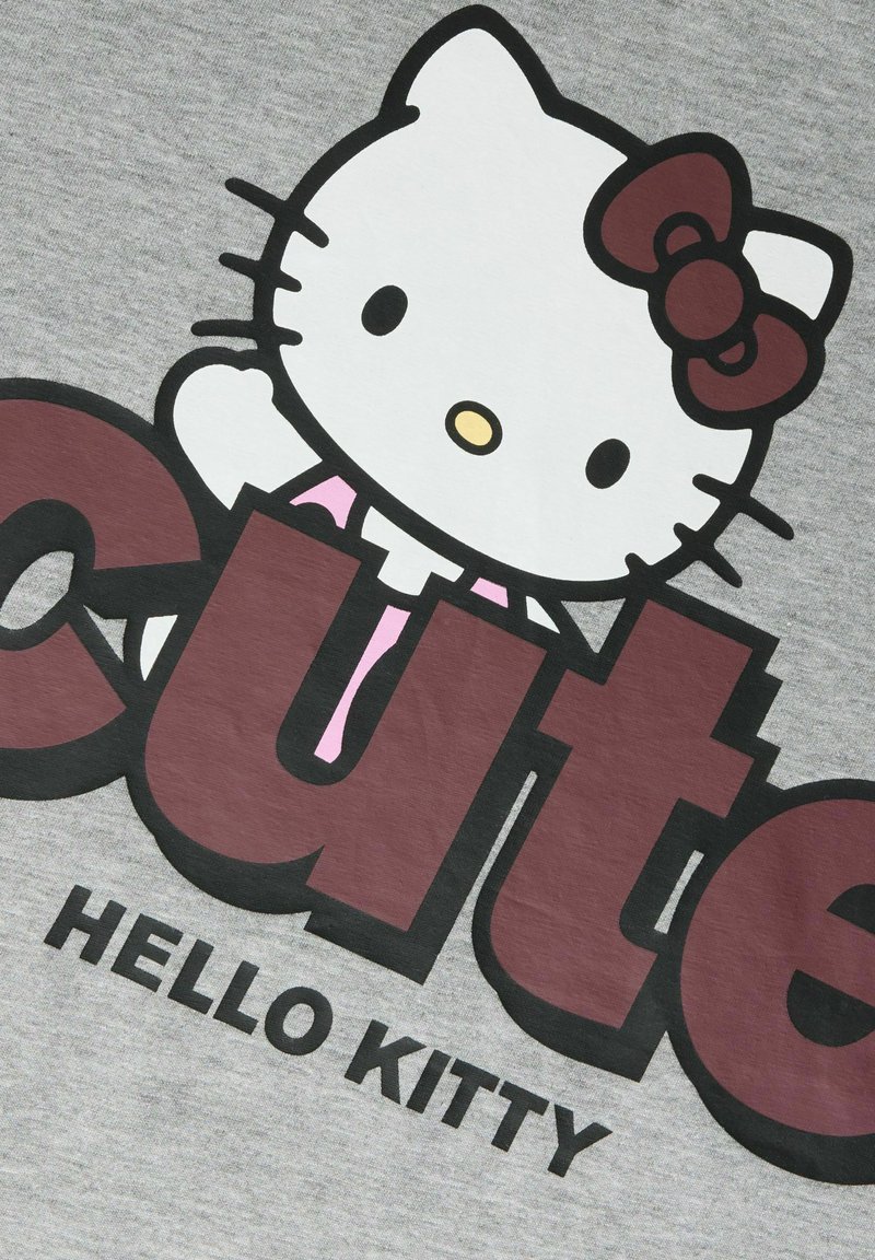 Χαρακτήρας Hello Kitty με κόκκινο φιόγκο και ροζ περιλαίμιο πάνω από μεγάλα, έντονα καφέ γράμματα που σχηματίζουν το "cute" σε γκρί ύφασμα.