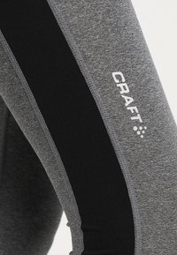 Grå träningsleggings med en svart sidpanel, tillverkade av elastiskt tyg med en slät yta. "CRAFT"-logotyp i vitt.
