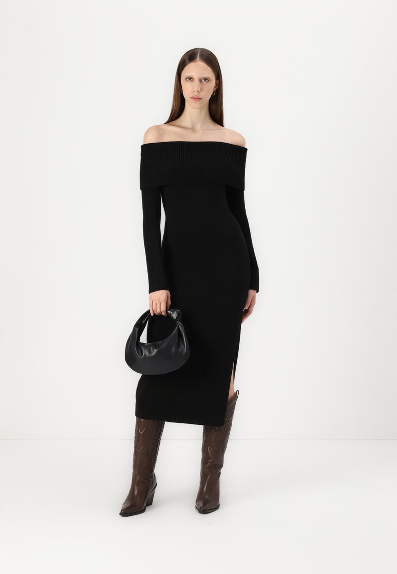 Schwarzes schulterfreies Kleid mit geripptem Muster, langen Ärmeln und seitlichem Schlitz. Kombiniert mit einer schwarzen Hobo-Tasche und braunen Absatzstiefeln.