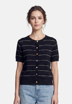 Donna che indossa un cardigan nero a maniche corte con sottili righe orizzontali e bottoni colorati, abbinato a jeans azzurri chiari.