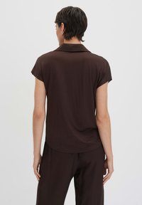 Chemise marron à manches courtes en tissu doux, avec un col classique, une coupe décontractée et un ourlet légèrement arrondi à l'arrière.
