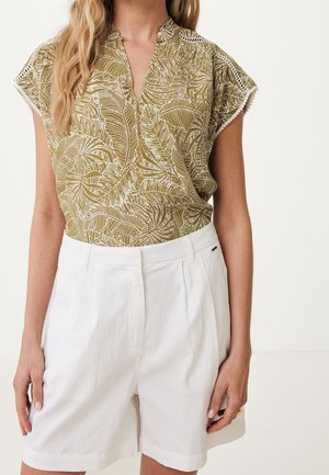 Femme portant un chemisier à manches courtes à motif de feuilles tropicales vert olive avec bordure en dentelle blanche et un short taille haute blanc.