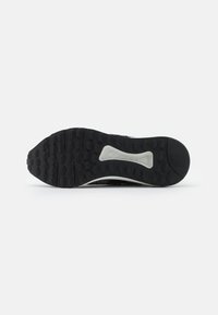 La semelle de la chaussure présente un fond en caoutchouc noir texturé avec des motifs circulaires, un talon renforcé et une semelle intermédiaire blanche pour un soutien supplémentaire.