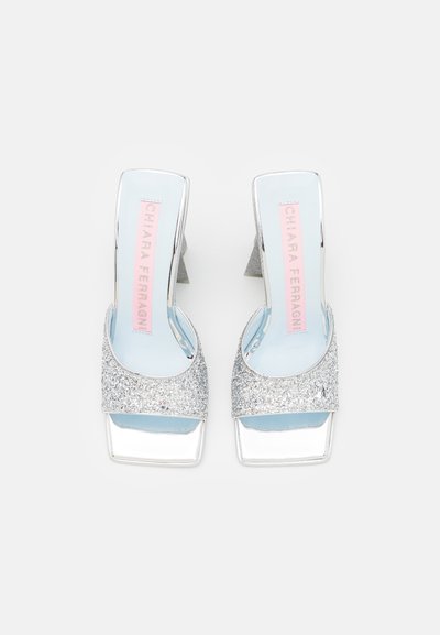 Sandales à talons hauts en paillettes argentées avec un bout carré et des accents métalliques brillants. Dotées d'un design à dos ouvert et d'une semelle intérieure bleu clair.