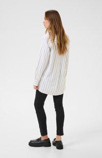 Long-sleeve, white shirt with light gray vertical stripes, paired with black skinny jeans and chunky black loafers. Smooth fabric texture.