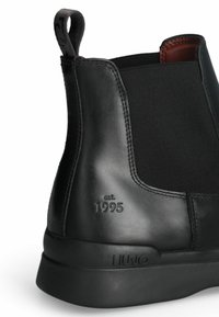 Stivale alla caviglia nero in pelle liscia con pannelli laterali elasticizzati, logo impresso e suola in gomma imbottita. Dettaglio data: dal 1995.