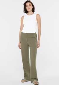 Leichte olivgrüne Hosen mit geradem Bein, ausgestattet mit einem Knopfverschluss und seitlichen Reißverschlusstaschen, kombiniert mit einem weißen Tanktop.