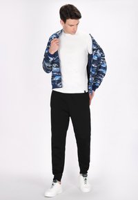 Blauwe en witte geblokte bomberjack over een wit T-shirt, gecombineerd met zwarte joggingbroeken en witte sneakers. Eenvoudige, casual sportkleding.