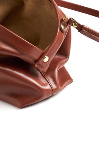 Bolso de cuero marrón con un diseño suave y arrugado. Presenta detalles de hardware dorado y una textura suave. El interior está forrado con un material más claro.