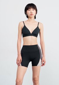 Brasiera sport neagră cu bretele subțiri și un design triunghiular, asortată cu șorturi negre cu talie înaltă, caracterizate prin accente gri pe laterale și o croială ajustată.