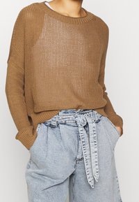 Maglione marrone lavorato a maglia con una vestibilità comoda e una texture a coste, abbinato a pantaloncini in denim blu chiaro a vita alta con cintura in tessuto.