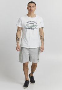 T-shirt en coton blanc avec les impressions "Blend Denim" et "Surfing". Shorts gris avec deux poches latérales, panneaux contrastants et chaussures noires.
