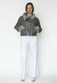 Harmaa nahkatakki, jossa on leveä kaulus ja pehmeä harmaa vuori. Takissa on napitus ja samansävyiset hihansuut, yhdistetty valkoisiin liehuviin housuihin.