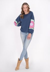 Felpa navy con maniche a motivo floreale in rosa, verde e lilla. Abbinata a jeans skinny blu chiaro e stivali da cowboy color cammello.