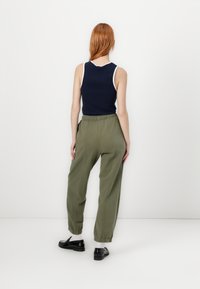 Marineblå ærmeløs top med hvid kant, parret med olivengrønne joggers med elastisk talje. Sorte sko med hvide sokker, set fra ryggen.