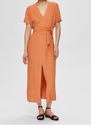 Pomarańczowa sukienka midi z krótkimi rękawami, dekoltem w serek i paskiem wiązanym w talii. Posiada przedni rozcięcie i gładką, lekką tkaninę. Czarne sandały na paski.