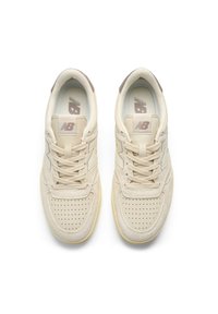 Pair of beige New Balance sneakers with perforated toe boxes and laces, viewed from above on a white background.