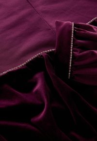 Hluboký purpurový samet s hladkou texturou, s nařízenými akcenty a zdobeným korálkovým lemem podél okrajů.