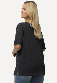 Černé oversized tričko s krátkými rukávy, s kulatým výstřihem, bočními rozparky a kontrastním prošíváním. Měkká, textured látka.