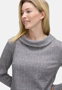 Top grigio a quadri con scollo drappeggiato, caratterizzato da un tessuto testurizzato e sottili accenti marroni nel motivo. Maniche lunghe visibili.