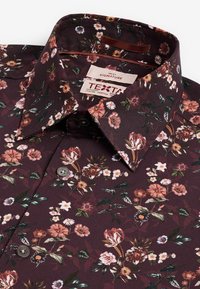 Bloemige shirt in donker bordeaux stof met een verscheidenheid aan bloemenpatronen. Beschikt over een klassieke kraag en grijze knopen. Merkal van het merk zichtbaar.