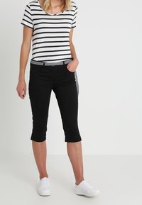 Svarta korta byxor med en åtsittande passform, kombinerade med en randig t-shirt i vitt och marinblått. Modellen bär vita sneakers och har en accent med ett nätbälte.