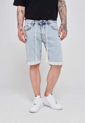 Shorts de mezclilla azul claro con dobladillos enrollados, cintura elástica con cordón, y bolsillos delanteros. Llevados con zapatillas blancas.