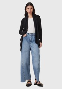 Black ribbed cardigan over a white T-shirt, paired with light blue wide-leg jeans. Black flats with gold hardware accents.