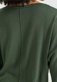 Oliwkowy sweter dzianinowy z detalem szwu z tyłu. Miękka tekstura, luźny krój i szeroki dekolt.