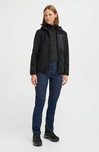 Veste en polaire noire avec fermeture éclair à l'avant et poche poitrine, associée à un pantalon cargo bleu marine avec panneaux au niveau des genoux et plusieurs poches.