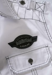 White fabric shirt with black stitching. Features an embroidered "Addicted" logo patch near the left pocket. Pocket has a rounded flap and button.