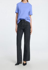 Jasnoniebieski bawełniany T-shirt w połączeniu z czarnymi dżinsami o wysokim stanie i szerokich nogawkach. Całość charakteryzuje się luźnym krojem i minimalistycznym designem.