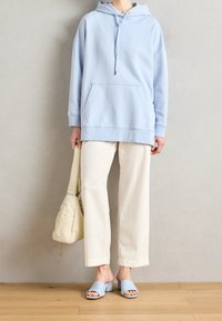 Hellblauer übergroßer Hoodie mit Kängurutasche, kombiniert mit cremefarbenen, weitem, geripptem Hosenbein und hellblauen Pantoletten.