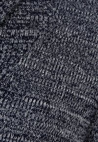 Tissu tricoté, bleu marine foncé avec des flecks gris clair, mettant en valeur un motif texturé avec des fils entrecroisés créant des crêtes et de la profondeur.