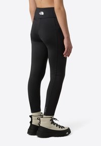 Čierne legíny s vysokým pásom a logom na zadnej strane. Hladká, pružná látka. V kombinácii so sivými turistickými topánkami s čiernymi detailmi.