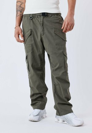 Pantalones cargo de color verde oliva con múltiples bolsillos laterales, cinturilla elástica y cinturón negro. Combinados con zapatillas blancas para un look casual.