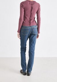 Top de canalé de manga larga color granate con detalle de volantes en la espalda, combinado con jeans de mezclilla azul que presentan un diseño clásico de bolsillo trasero. Bailarinas negras con tachuelas.