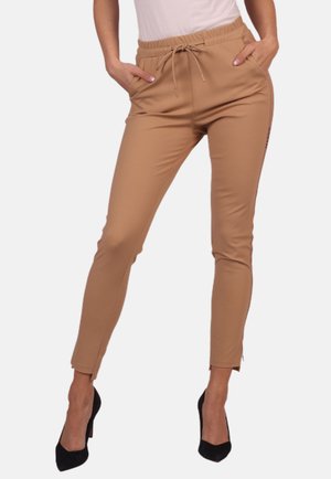 Beige schmal zulaufende Hosen mit einem Kordelzugbund, seitlichen Taschen und Schlitzen an den Knöcheln, aus glattem Material. Mit Logo-Detail akzentuiert.