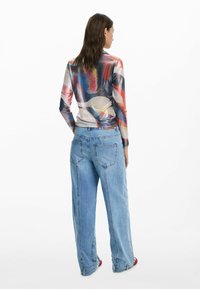Long-sleeve, multicolored top in sheer, shiny fabric, paired with high-waisted, loose-fitting blue denim jeans featuring large pockets.