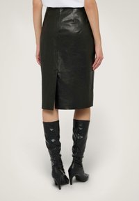 Schwarzer Leder-Midi-Rock mit gerader Silhouette, Rückenschlitz und hochtailliertem Schnitt. Verfügt über eine glatte Textur und einen subtilen Glanz.