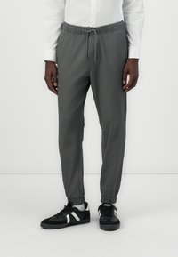Gray tapered joggers made of soft fabric, featuring an elastic waistband, adjustable drawstring, and elastic cuffs, paired with black sneakers.
